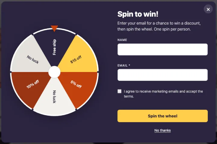 A popup over a dimmed shop page. On the left, a prize wheel with slices for Free ship, $15 off, 5% off, No luck, 10% off and No luck. On the right, the heading Spin to win!, a short description, Name and Email fields, a marketing consent tick box, a yellow Spin the wheel button and a No thanks link.